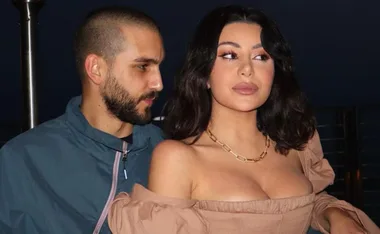 Couple posing at night; woman in beige dress, man in blue jacket, both looking right.