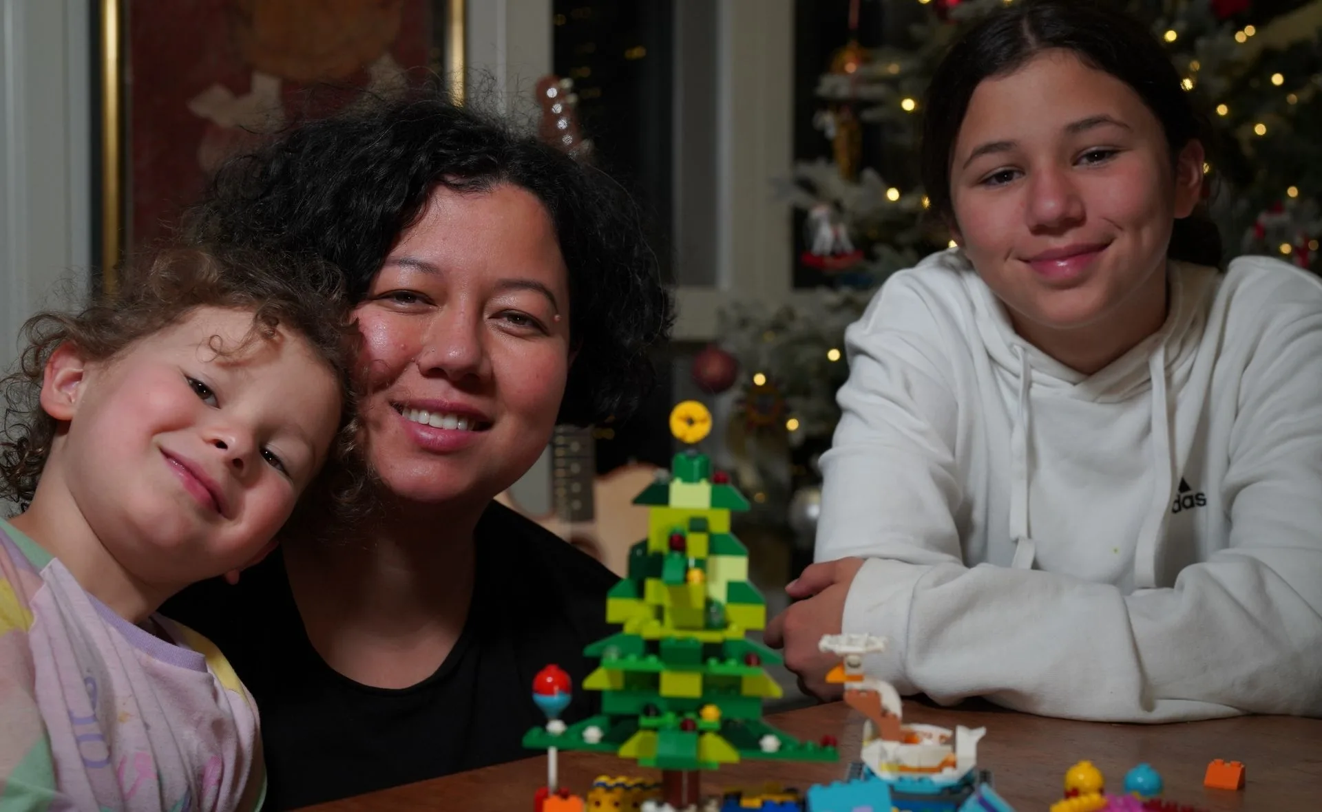 A family smiling by a Christmas tree with Lego decorations on the table in front.