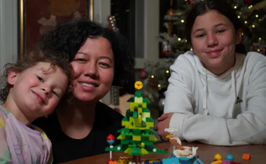 A family smiling by a Christmas tree with Lego decorations on the table in front.