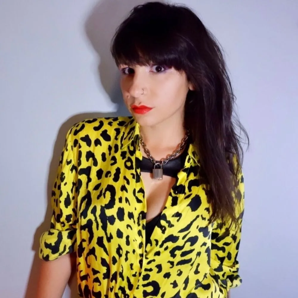 Woman in a yellow leopard print top and red lipstick against a plain background.