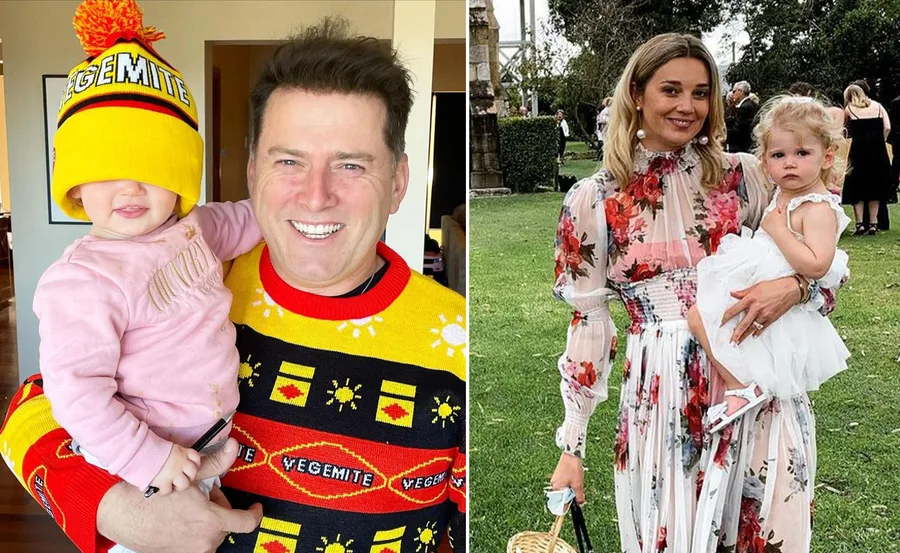 Man in Vegemite sweater holds child, woman in floral dress holds a toddler in a garden.