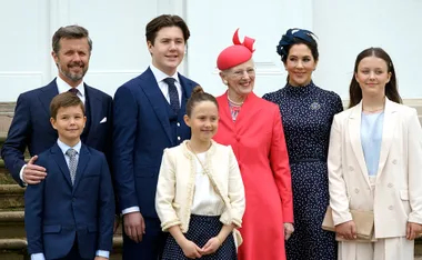 A royal family poses together, dressed elegantly, with one member in a bright red suit and hat.