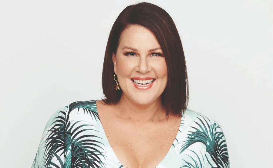 Smiling woman with short brown hair, wearing earrings and a leaf-patterned top.
