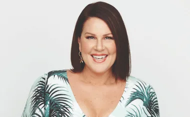 Smiling woman with short brown hair, wearing earrings and a leaf-patterned top.