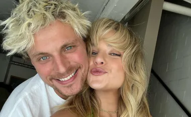 Happy couple with blonde hair smiling and posing cheek-to-cheek for a selfie indoors.