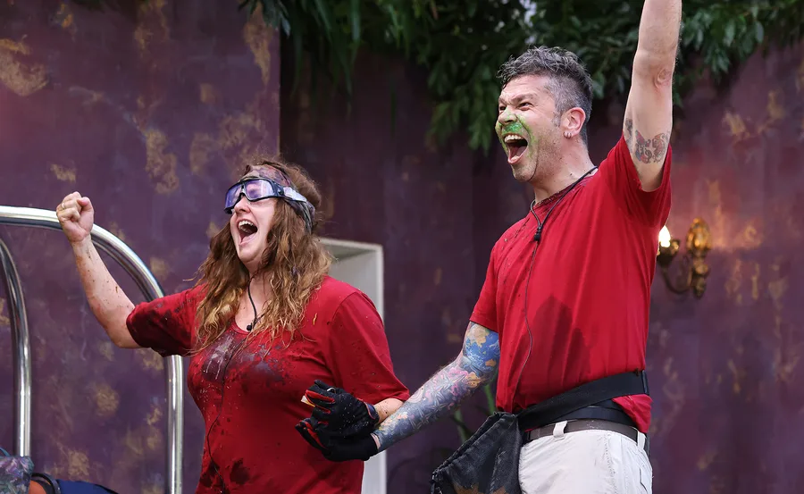 Two people in red shirts celebrate enthusiastically, both visibly messy with joy, indoors with purple walls.