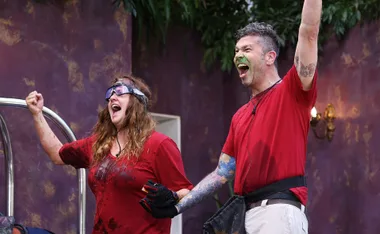 Two people in red shirts celebrate enthusiastically, both visibly messy with joy, indoors with purple walls.
