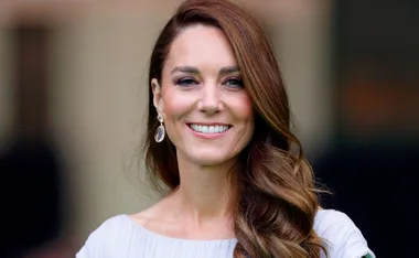 A woman smiling with long brown hair and elegant earrings in a portrait setting.