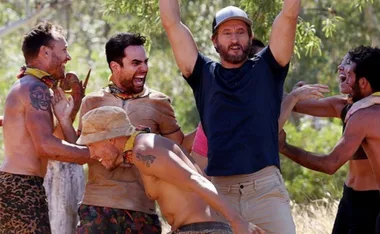 Group of people celebrating outdoors, one person with arms raised, others with smiles and laughter, wearing tribal-themed accessories.