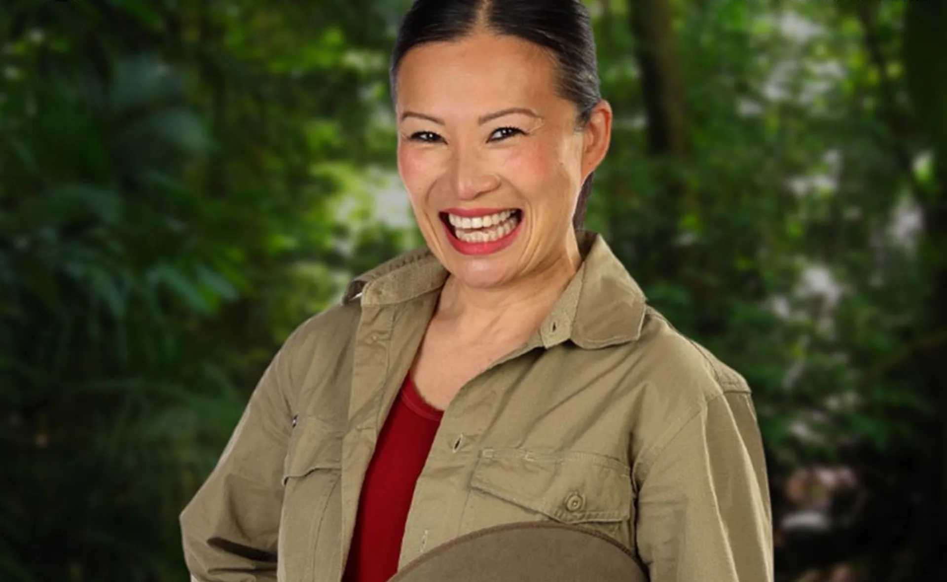 A person smiling broadly, wearing a khaki shirt, outdoors with greenery in the background.