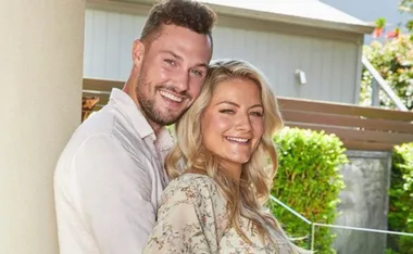 Couple smiling and embracing outdoors, greenery in the background.