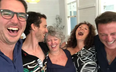 Group of five people laughing together at a celebration indoors.