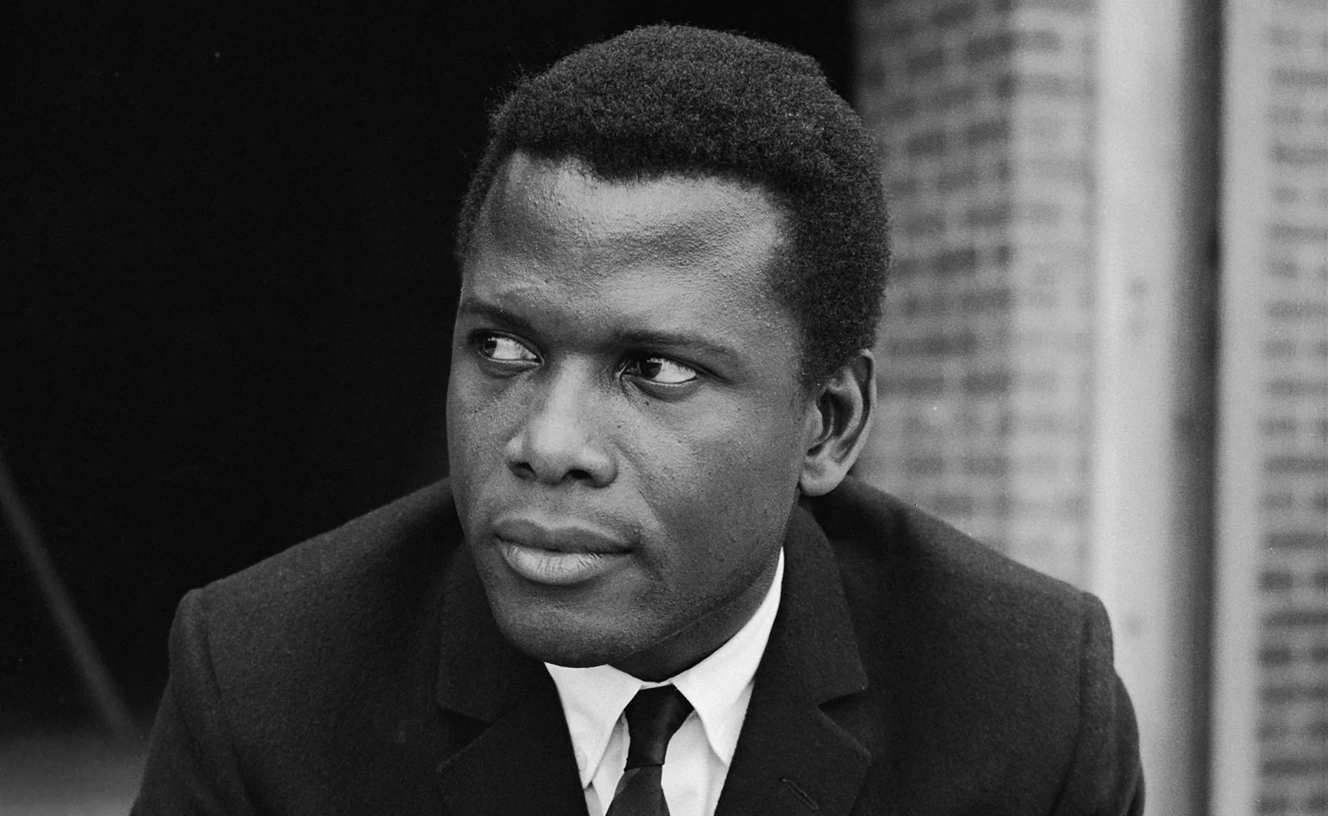 A black and white image of a man in a suit looking to the side, with a thoughtful expression.