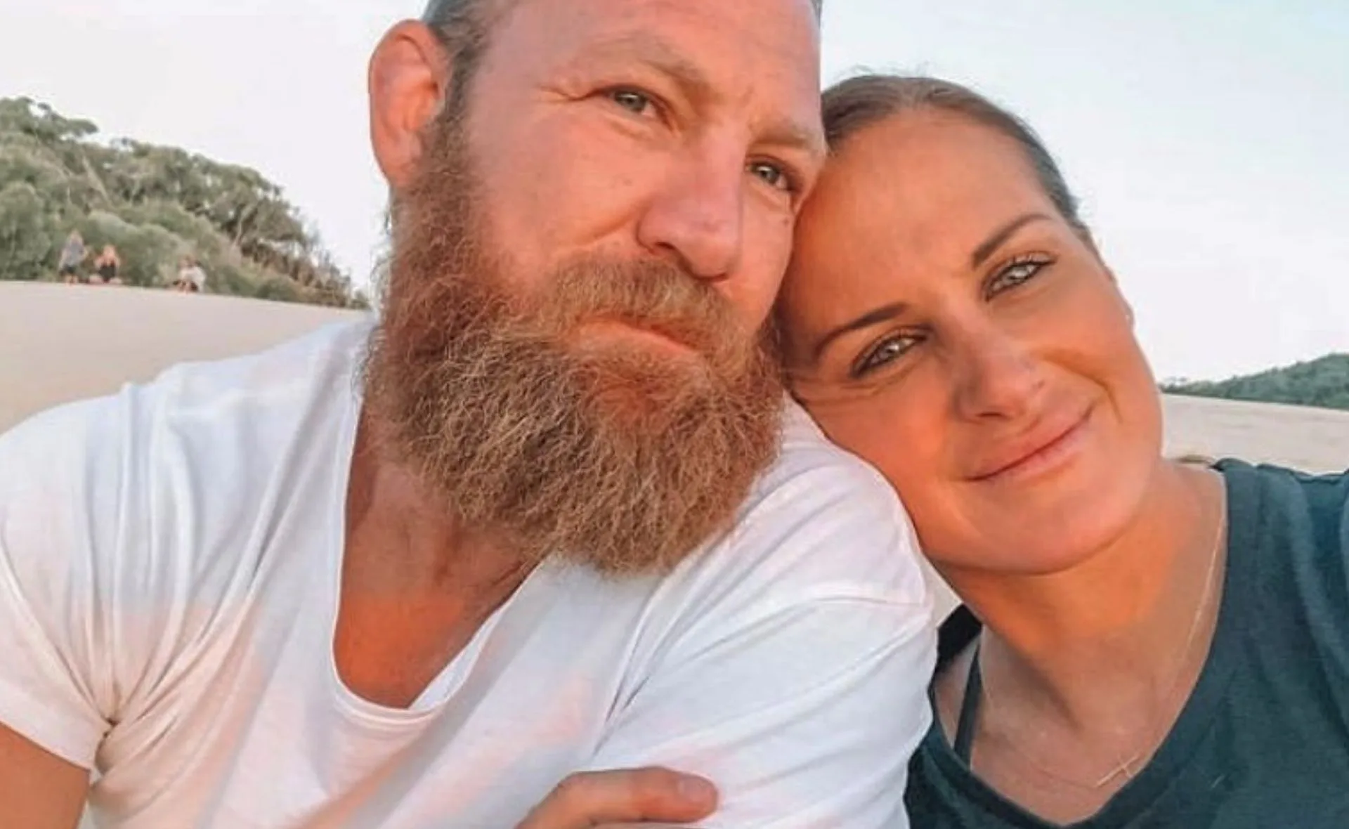 A couple smiling together outdoors, with trees in the background.