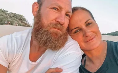 A couple smiling together outdoors, with trees in the background.