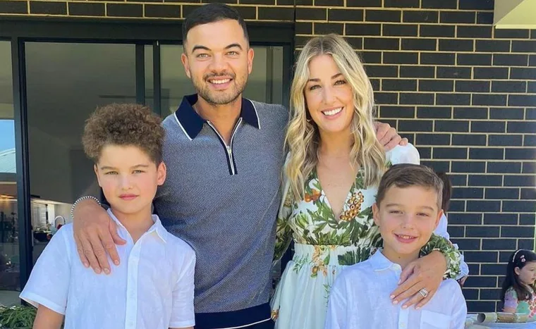 A family of four poses together outdoors, smiling, with the parents in the middle and two children on either side.