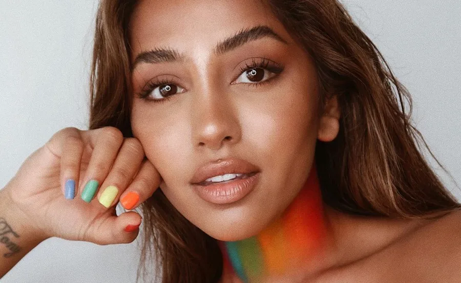 A woman with colorful rainbow nails and neck, gazing directly, showcasing diversity and pride.