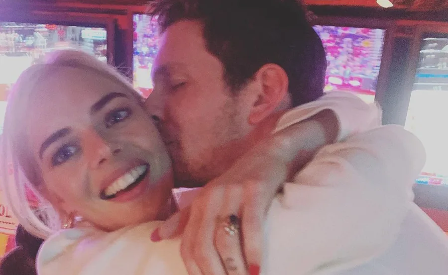 A couple embracing and smiling at a sports event with screens in the background.