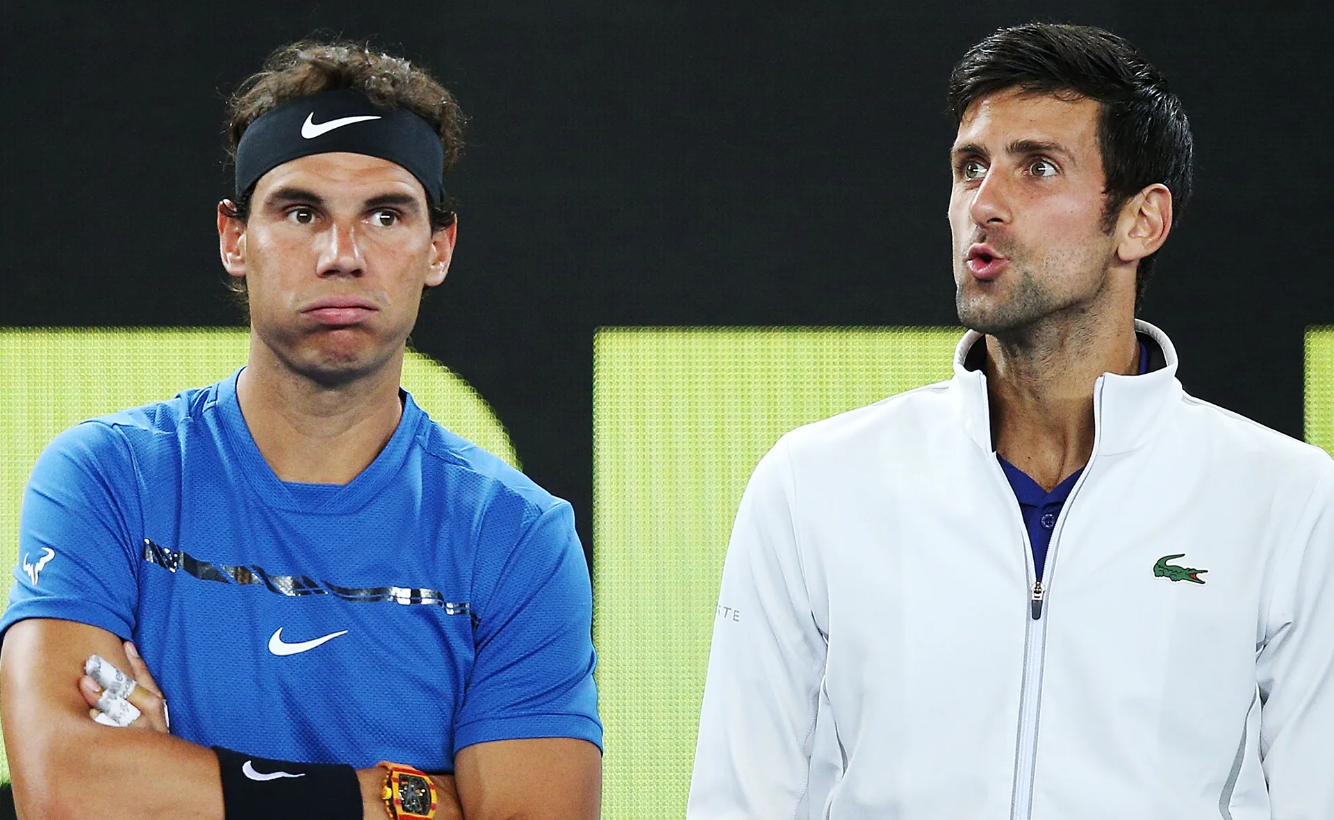 Two tennis players express different emotions on a court, one in blue shirt, the other in white jacket, both focused.