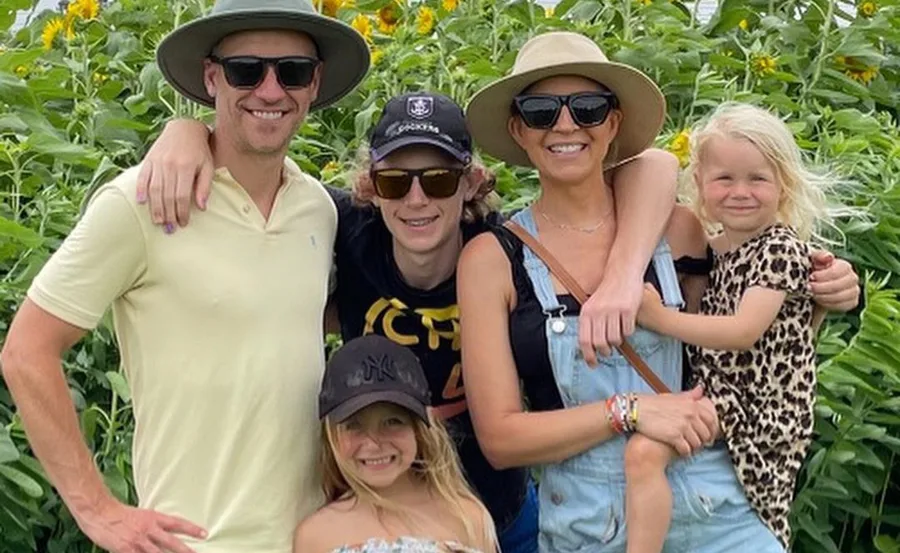 Family posing together in front of sunflowers, all wearing hats and sunglasses.