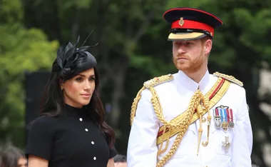 Prince Harry in military uniform and Meghan Markle in black dress with hat, attending a formal event outdoors.