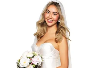 A smiling bride in a white dress with a veil, holding a bouquet of white and pink flowers.