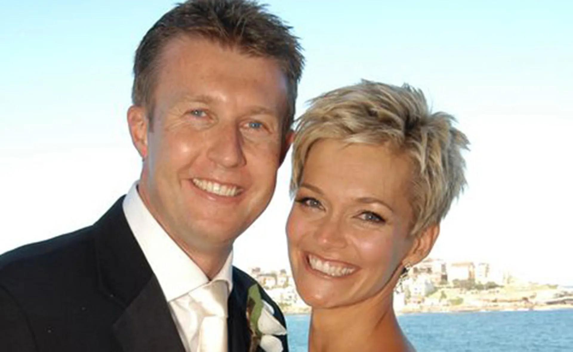 Smiling couple posing outdoors with a scenic background.