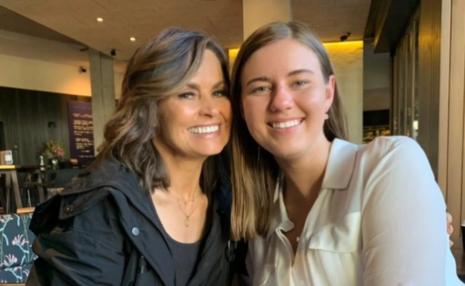 Two women smiling together in a warmly lit indoor setting.