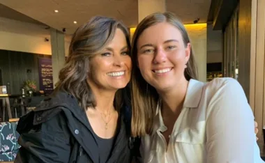 Two women smiling together in a warmly lit indoor setting.