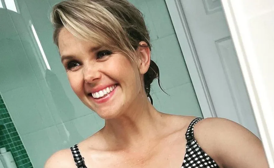 Smiling woman taking a selfie in a bathroom, wearing a checkered top.