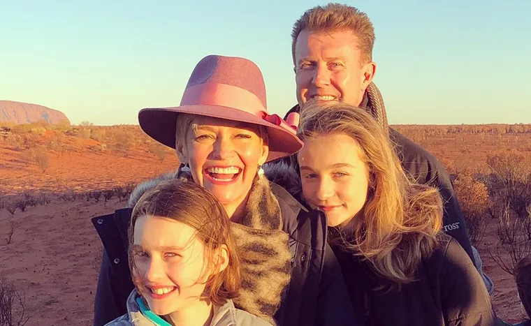 A family smiling together in a desert landscape during sunset, with a prominent rock formation in the background.