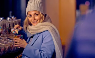Woman in a hat and scarf smiles while scooping candy from a dispenser.