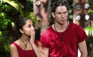 Two people in red shirts, one covering their mouth, standing outside with a serious expression.