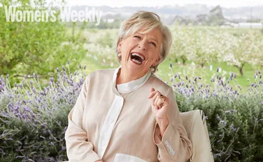 Elderly woman joyfully laughing in a garden setting with lavender and greenery; "Women's Weekly" text in corner.