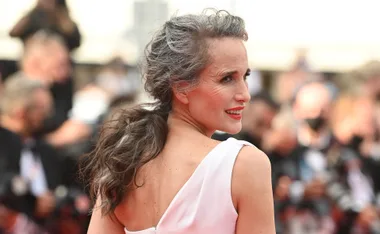 Elegant woman with grey hair in an updo and white dress at an event, smiling over her shoulder.