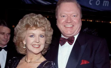 A smiling couple in formal attire with a man wearing a bow tie and a woman in earrings at an event.