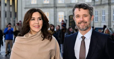 Couple smiling outdoors with a crowd in the background, both dressed formally.