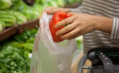 Person placing a red bell pepper into a plastic bag in a grocery store.