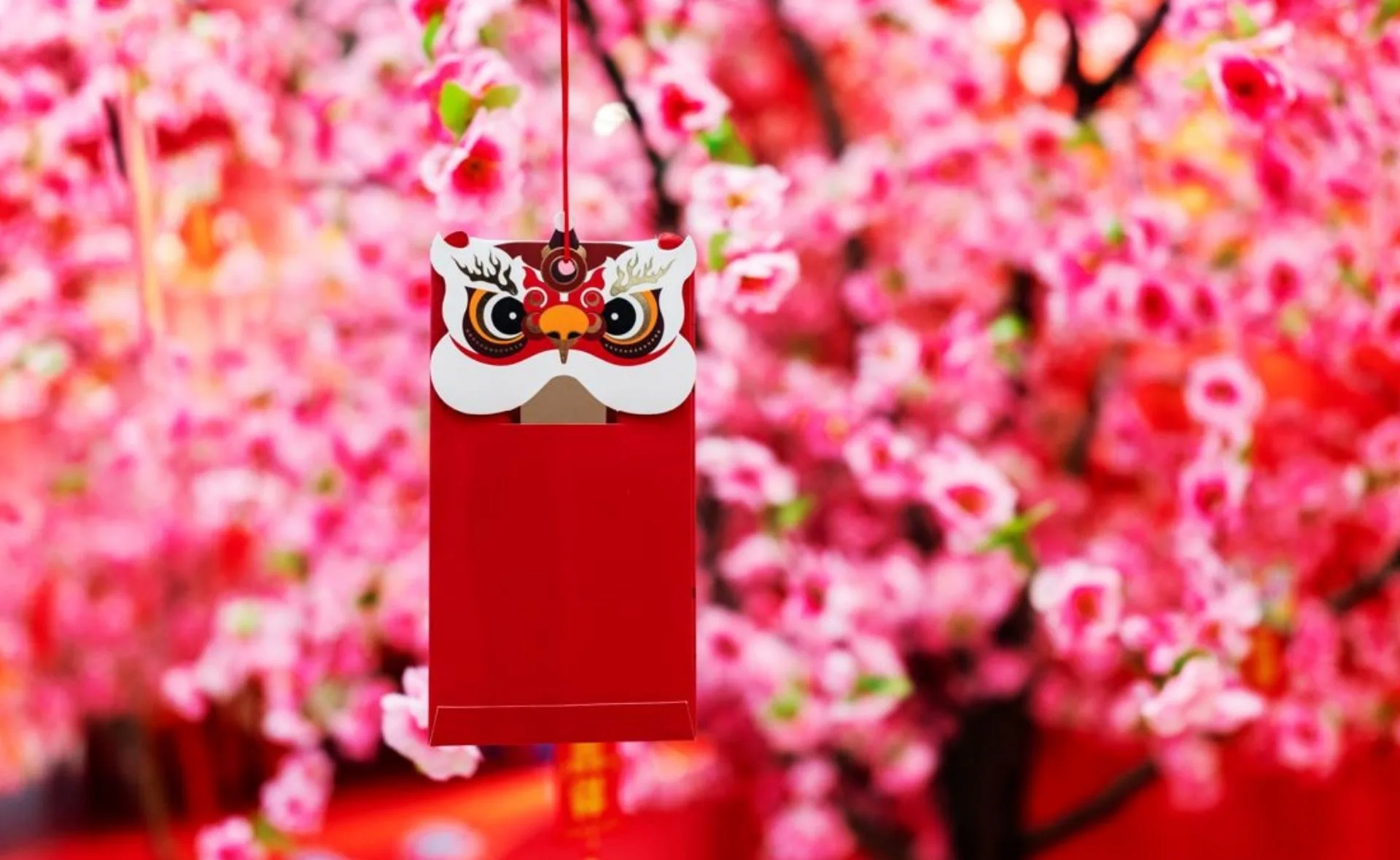 Red envelope with dragon design hanging among pink cherry blossoms, celebrating Lunar New Year.