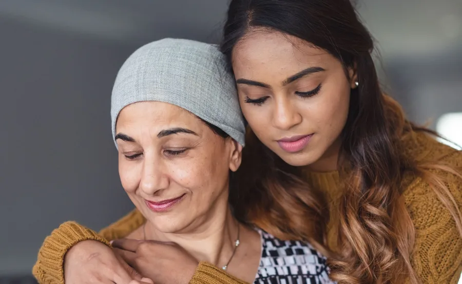 A young woman comforting an older woman wearing a headscarf, symbolizing support during illness.