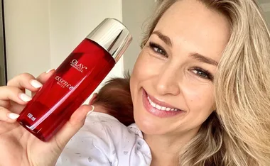Smiling woman holding a bottle of Olay Regenerist Essence Water.