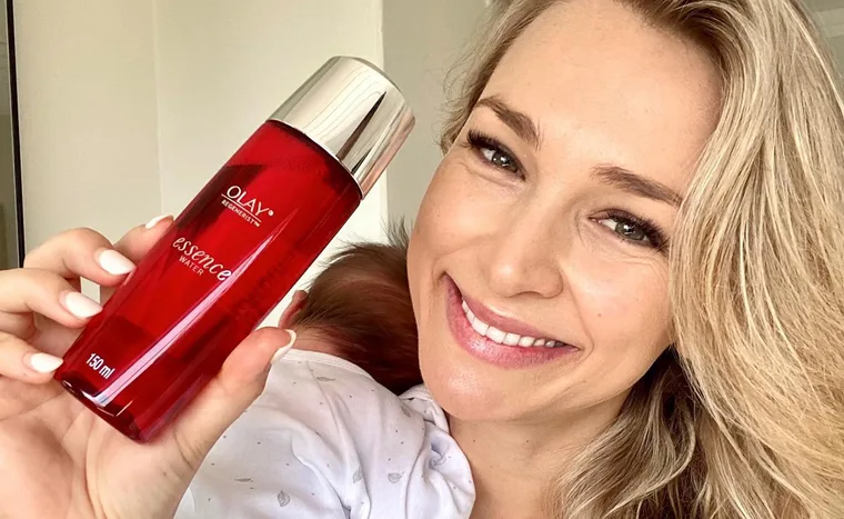 Smiling woman holding a bottle of Olay Regenerist Essence Water.