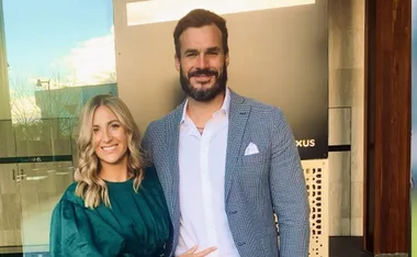 A smiling couple poses together, with the woman in a green dress and the man in a patterned suit jacket.