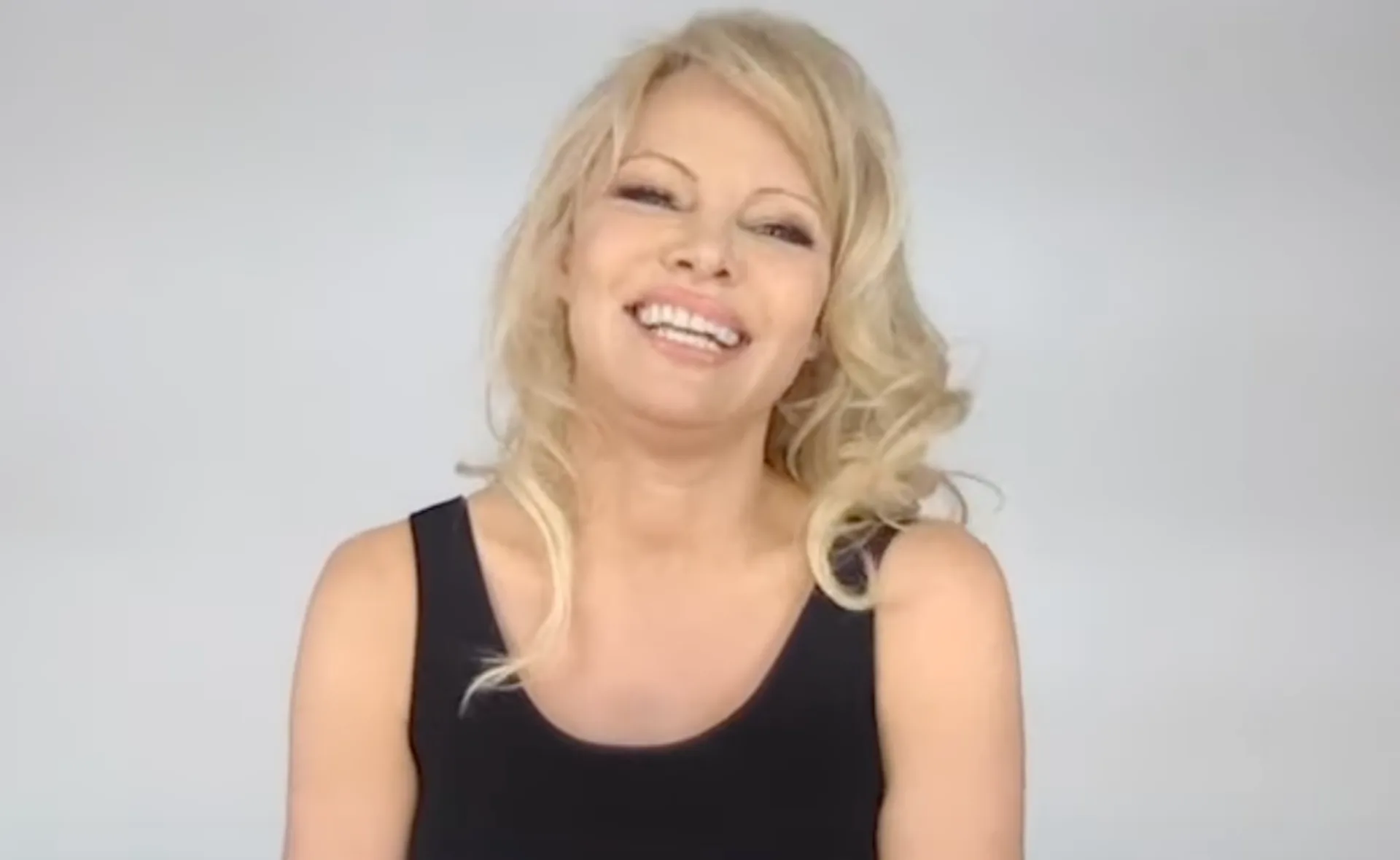 A person with blonde hair smiling, wearing a black top against a plain background.