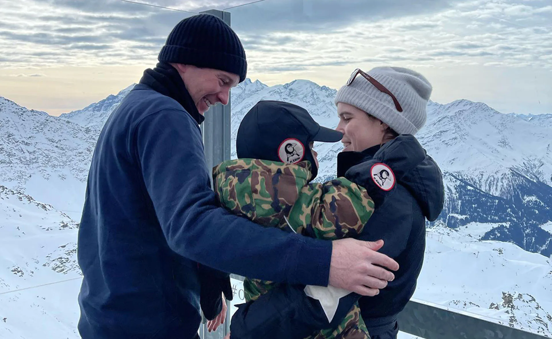 Family enjoying snowy mountain views, bundled warmly, smiling and hugging against a scenic backdrop.