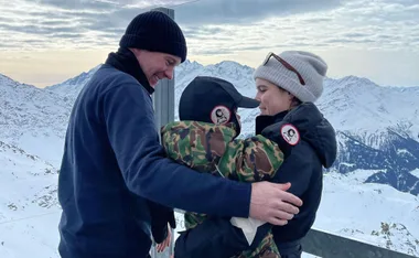Family enjoying snowy mountain views, bundled warmly, smiling and hugging against a scenic backdrop.