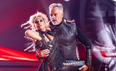 A man and woman in stylish dance costumes perform on stage with dramatic lighting.