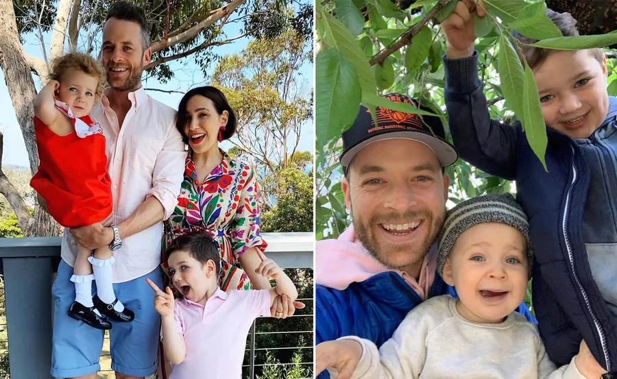 A happy family smiling outdoors, with a man, woman, and two children posing among trees.