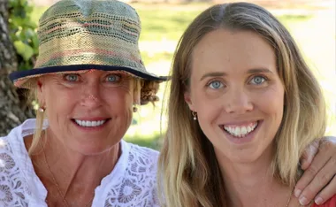 Two smiling women outdoors, one in a hat; both with blue eyes and light hair.