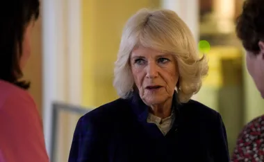A woman with short blonde hair speaks with two people in a softly lit indoor setting.